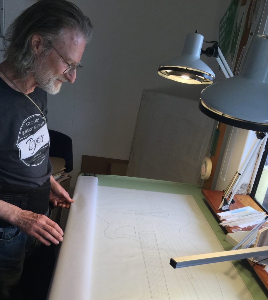 Man examining guitar blueprint under lamp.