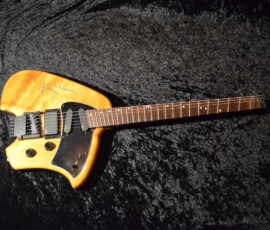 Wooden electric guitar on dark fabric background.