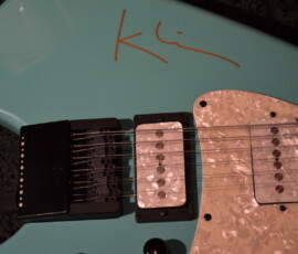 Turquoise electric guitar with signature on body.