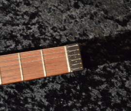 Guitar fretboard on textured dark surface.
