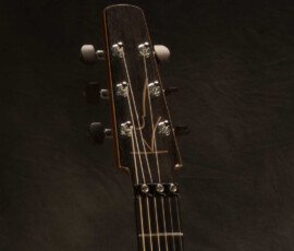 Acoustic guitar headstock against dark background.