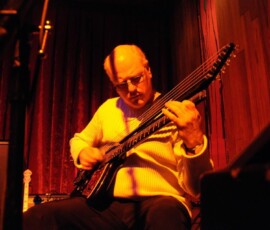 Musician playing guitar on dimly lit stage.